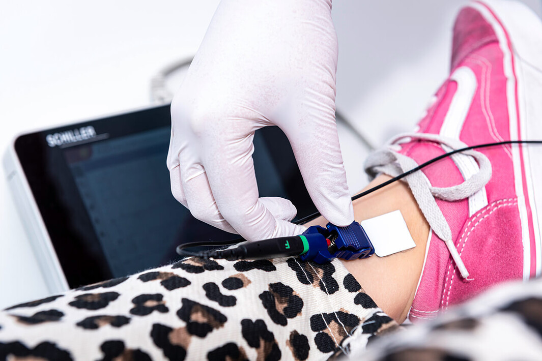 Kind mit Turnschuhen erhält ein EKG, eine medizinische Fachkraft legt Elektroden am Bein an.